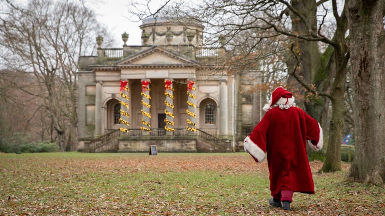 Father Christmas in his traditional red coat walking towards Gibside Chapel, with the column decorated with lights.